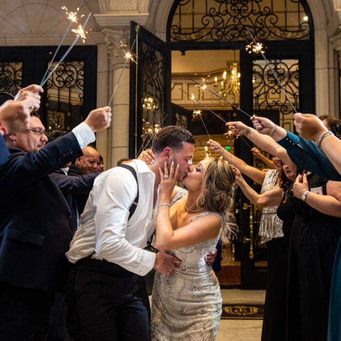 bride and groom kissing with wedding party celebrating